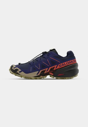 Buty do biegania w terenie z purpurową syntetyczną cholewką, czarnymi detalami, pomarańczowymi akcentami oraz wytrzymałą podeszwą zapewniającą przyczepność. Wyposażone w system szybkiego sznurowania.