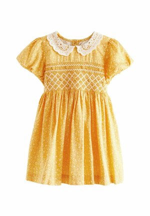 Robe jaune pour enfant avec motifs floraux blancs, corsage smocké, manches bouffantes et col en dentelle blanche de style Peter Pan.