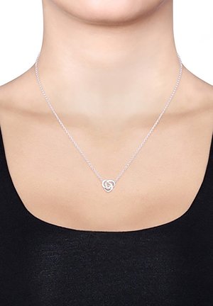 Silberne Halskette mit einem verdrehten runden Anhänger, versehen mit einer zarten Kette und einer polierten Oberfläche, getragen über einem schwarzen Oberteil.