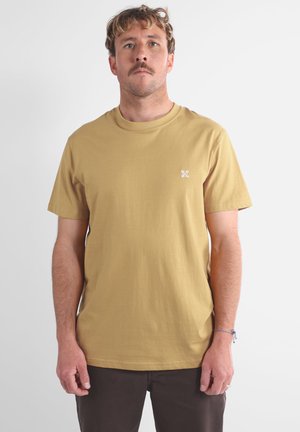 T-shirt en coton léger marron clair à manches courtes avec un col rond ; présente un petit logo blanc sur le côté gauche de la poitrine et une coupe décontractée.