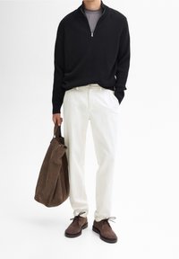 Black ribbed zip-up sweater, white trousers, brown suede shoes, and a brown fabric tote bag. The outfit presents a neutral color palette.