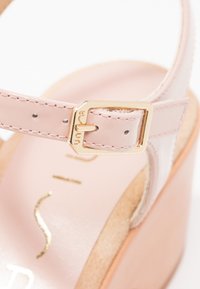 Sandale en cuir verni rose avec une boucle en or, une plateforme en liège et une bride en cuir lisse. Branding doré notable sur la semelle intérieure.