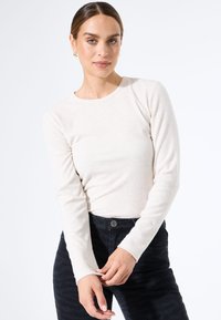 Langarm, lichtbeige geribde top gecombineerd met donkere gestructureerde jeans. Strak ontwerp met een ronde halslijn en slanke mouwen.