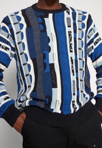 Pull en tricot bleu et blanc avec un motif rayé vertical, des accents texturés, et un col et des poignets côtelés.