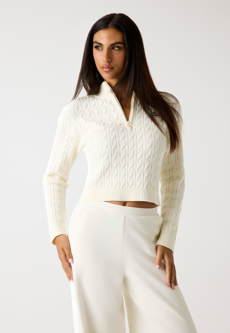 Maglione a lavorazione a trecce, con zip, di colore crema e dalla vestibilità cropped. Presenta maniche lunghe e orlo a coste. Abbinato a pantaloni bianchi a vita alta coordinati.