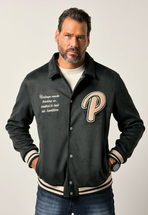 Zwarte suède varsity jas met beige strepen, geborduurde letter "P," en tekstdetail aan de linkerzijde. Voorzien van drukknoopsluiting en geribde manchetten.