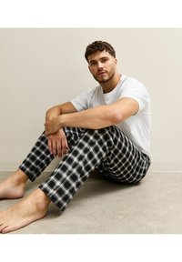 Black and white plaid pajama pants with a soft texture, paired with a plain white T-shirt. The individual sits on a light gray surface.