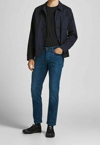 Navy button-up jacket over a black t-shirt, paired with blue jeans and black sneakers. Features include a chest pocket and plain texture.