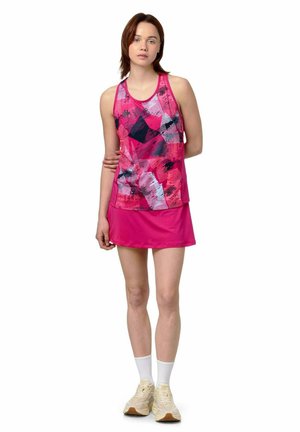 Femme debout portant un haut sans manches rose à motif abstrait et une jupe rose assortie avec des chaussettes blanches et des baskets beiges.