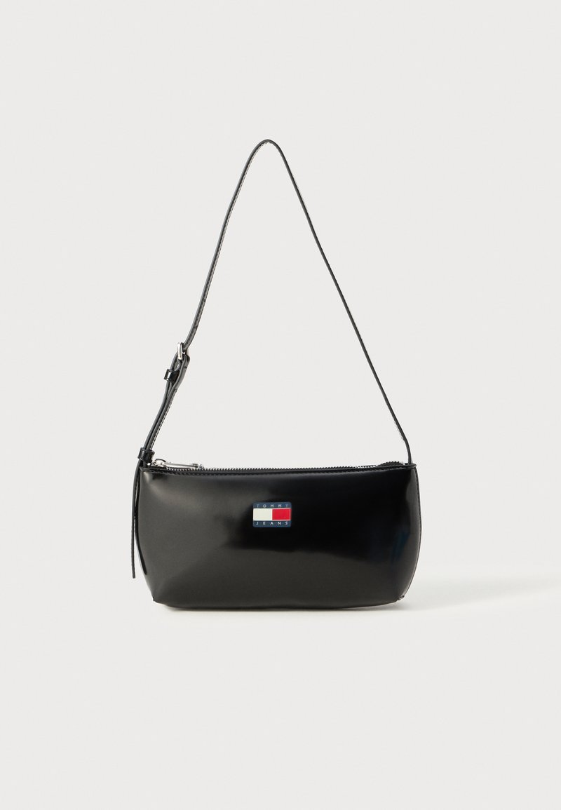 Black patent leather crossbody bag with a zip closure, featuring a logo patch in red, white, and blue, and a thin adjustable strap.