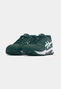 Σκούρα πράσινα αθλητικά παπούτσια με υφή στο πάνω μέρος, λευκές λεπτομέρειες, μαλακό γιακά και λαστιχένια σόλα για καλύτερη πρόσφυση. Ορατά τα κορδόνια και το λογότυπο.