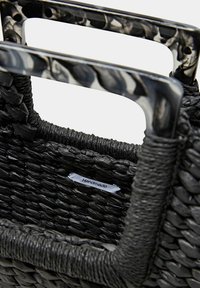 Borsa intrecciata nera con materiale testurizzato, manici decorati con motivo e etichetta "Fatto a mano". Accenti lisci e lucidi completano il design.