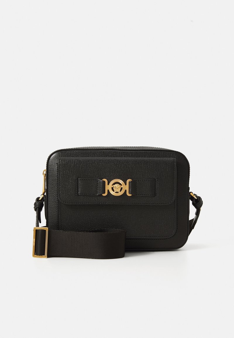 Geantă crossbody din piele texturată neagră, cu clapetă frontală, închidere cu emblema Medusa aurie și curea fabrică reglabilă lată cu cataramă aurie.