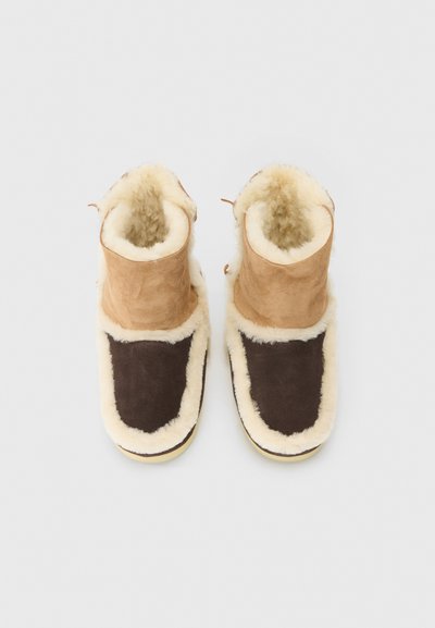 Botas de ante marrón y beige con forro de borreguillo color crema. Cuello redondeado, costuras reforzadas y suela plana.