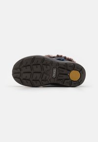 Suela de zapato de goma negra con un patrón de agarre texturizado y una etiqueta circular con logotipo; los bordes son curvos, con un acento de piel marrón en la parte superior.