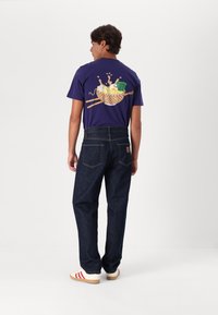 Camiseta púrpura con un gráfico de un tazón y fideos. Combinada con jeans de mezclilla oscura y zapatillas crema con rayas rojas.