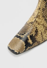 Κοντινό πλάνο σε μποτάκι με μυτερή μύτη, με υφή από δέρμα φιδιού σε μπεζ και μαύρο και λεπτομερή μοτίβο από λέπια.