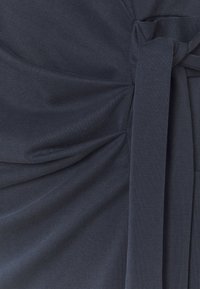 Tmavě námořnické šaty s texturovanou tkaninou, sklady, detailem na vázání v pase a hladkým, jemným povrchem.