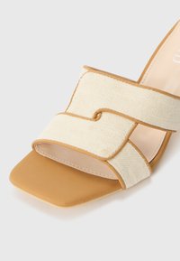 Beige fabric slide sandal with a textured upper, rounded crossover straps, and a tan rubber sole, featuring a square toe design.