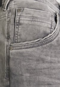 Jeans de mezclilla gris con un acabado desteñido, que cuentan con un bolsillo frontal con herrajes metálicos y detalles de costura sutiles a lo largo de los bordes.