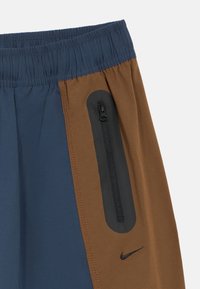 Σορτς Nike με μπλοκ χρωμάτων σε μπλε και καφέ, ελαστική μέση, πλαϊνή τσέπη με φερμουάρ και μαύρο εξάρτημα, με ομαλή υφή.