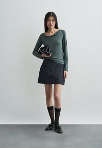 Zielony top z długim rękawem i marszczonym dekoltem; ciemnoniebieska spódnica dżinsowa; czarna lakierowana torebka; czarne skarpetki do kolan; czarne płaskie buty.