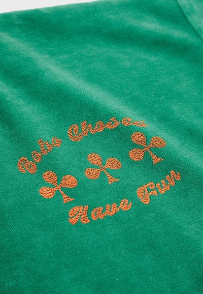 Grüner Sweatshirt mit orangefarbener gestickter Aufschrift "Choose Fun", umgeben von vier Kleeblatt-Motiven, mit einer strukturierten Stoffoberfläche.