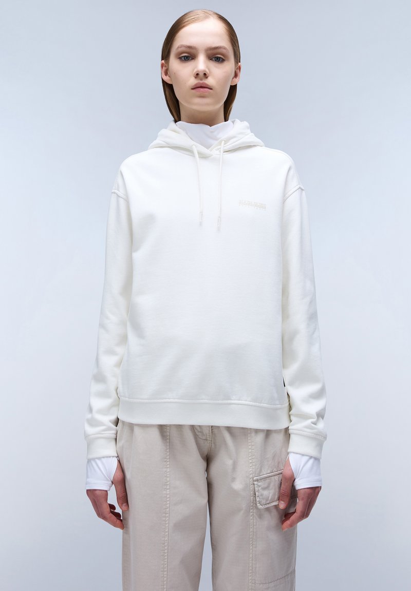 Felpa bianca con cappuccio e un logo discreto sul petto. Il tessuto è liscio, abbinato a pantaloni beige chiaro.