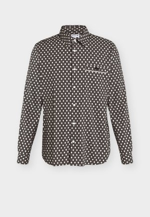 Chemise noire à manches longues boutonnée, motif géométrique blanc, col pointu, poche poitrine avec bordure blanche et boutons blancs visibles sur le devant.