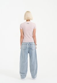 Fitted light pink t-shirt with short sleeves, featuring a black logo on the back; paired with loose blue denim jeans and white sneakers.