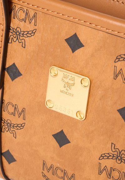 Sac en cuir marron clair avec logos MCM noirs et une plaque en métal doré gravée « MCM München » et le numéro de série 85351.