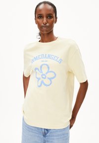 Gelbes Baumwoll-T-Shirt mit kurzen Ärmeln, mit einem blauen Blumenmotiv und dem Text "ARMEDANGELS" darüber. Das Model trägt eine Jeansshorts.