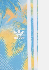 Adidas-shorts i lyseblå med et palmetre-mønster, som har hvite vertikale striper og et hvitt Adidas-logo.