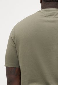 Zielonooliwkowy t-shirt z krótkim rękawem wykonany z miękkiego materiału, z okrągłym dekoltem i gładką fakturą, z przeszyciami na ramionach.