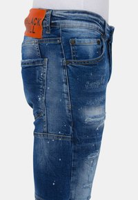 Denim jeans in een medium blauwe wast met verwerkte details, witte spetteraccenten en een oranje leren achterpatch met het label "BLACK BULL."