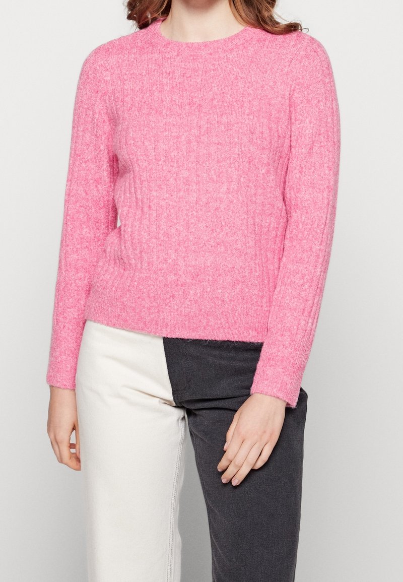 Rosa ribbad stickad tröja med långa ärmar och rundad halsringning. Tyget verkar mjukt med en strukturerad yta.