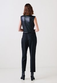 Top senza maniche nero con finitura lucida, abbinato a pantaloni neri a righe; cintura regolabile, due tasche posteriori e stivaletti con tacco.