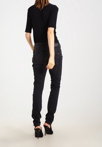 Černý přiléhavý top s krátkými rukávy, v kombinaci se slim-fit tmavými džíny. Vysoké podpatky zdůrazňují outfit. Jednoduchá, hladká textura po celém povrchu.