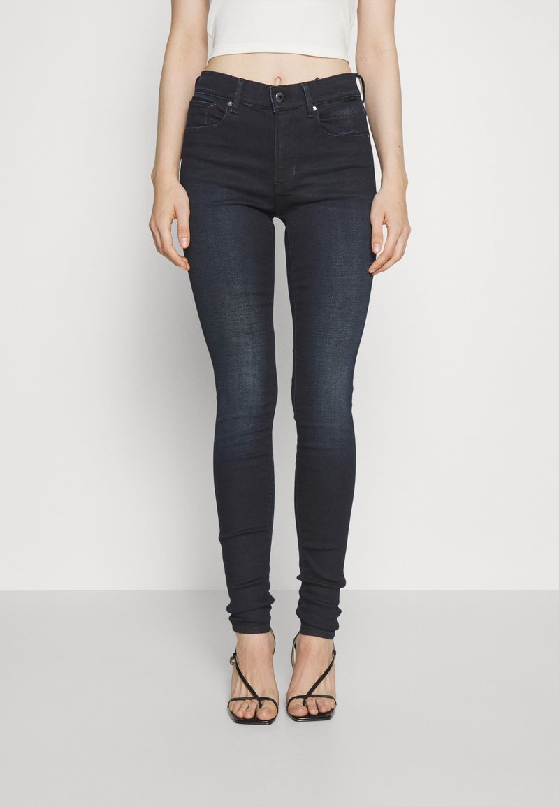 Jeans skinny taille haute bleu foncé avec une texture en denim lisse et extensible. Comprend des poches avant et un design classique à cinq poches.