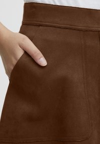 Brown suede skirt with a smooth texture; features a side pocket and visible stitching details along the seams and waistband.