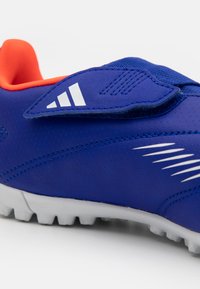 Zapatilla deportiva sintética azul con vibrante interior naranja, superficie texturizada, acentos blancos y suela estriada distintiva para mayor agarre.
