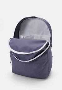 Mochila azul oscura con bolsillo frontal con cremallera y compartimento principal grande abierto, mostrando el forro interior gris claro.