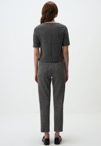 Completo in maglia grigio a due pezzi con maniche corte e pantaloni su misura. TessutoTesturizzato con leggera lucentezza e dettagli di design sottili. Scarpe nere.
