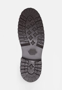 Suola di scarpa in gomma nera con un design di battistrada robusto, caratterizzata da texture variabili e un accento esagonale al centro.