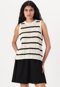 Pull sans manches en crème avec des rayures noires. Comprend un design ajouré, un col en côte et un tissu texturé. Assorti à une jupe noire.