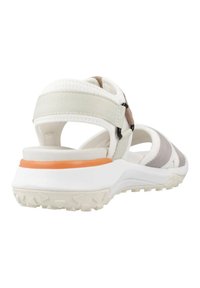 Sandalia atlética blanca con correas grises y beige, parte trasera ajustable, suela texturizada y un acento naranja en el mediopie que contrasta.