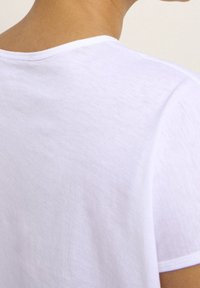 T-shirt bianco in cotone, vestibilità relax, cucitura del collo visibile, texture morbida, design minimale, silhouette ben definita.