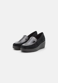 Zwarte suède instapschoenen met een glanzend zwart lakleren voorkant, voorzien van een wiggenhak, ronde neus en minimale stiksel details.