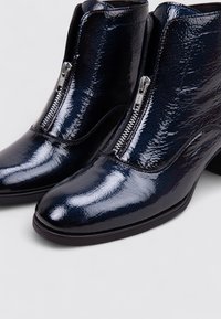 Bottes chelsea en cuir verni bleu marine avec un bout pointu, des coutures subtiles et une fermeture à glissière latérale en argent. Design à petit talon carré.