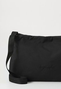 Black fabric shoulder bag with a smooth texture, adjustable strap, and embossed logo. Simple, rectangular design without additional patterns.